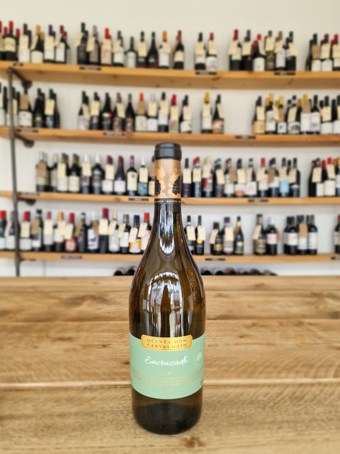 Wine bottle with a green label on a wooden surface, with a wine rack in the background.