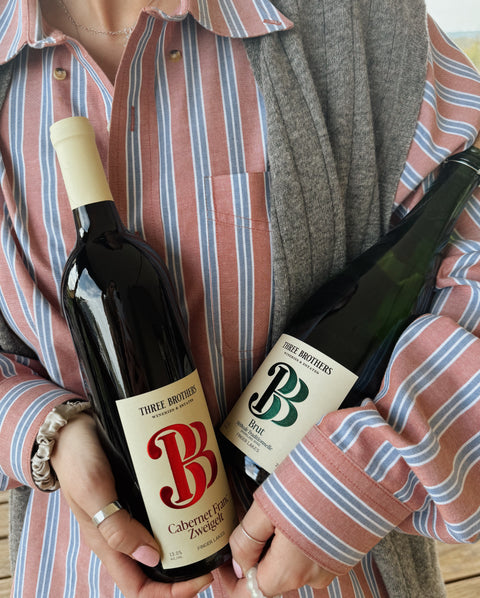Two bottles of Three Brothers wine held by a person wearing a striped shirt.